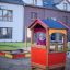 Barn leker i et Kiosk-lekehus på en lekeplass foran boligblokker.