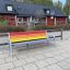 Colourful bench med metallramme og flerfargede treplanker plassert på fortau ved boligområde.
