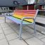 Colourful bench med regnbuefargede treplanker og metallramme på lekeplass.