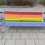 Colourful bench i regnbuefarger med metallramme på fortau.
