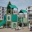Tårn lekehus med rutsjebane i grønt og grått på lekeplass med barn som leker.