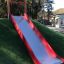 Rød Slide sklie plassert på en gressdekket høyde i en lekepark.