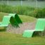 Lounge Stol i grønt metall plassert på lekeplass med gress og planter.