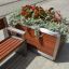 Bohus blomsterramme med røde blomster og grønne planter ved benk.